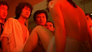 Angel Guts Nami 1979 exhibition scene. Nude woman seen from the back while standing before men under strong red light in a room.