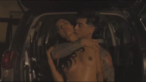 Topless and shirtless car sex scene from Booking (2026) - intimate embrace in the open trunk of an SUV.