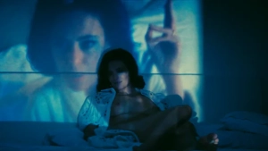Jasmine Trinca nude scene in Gli occhi degli altri 2025 - actress lying on bed with blue-lit projected figure behind her wearing sheer robe looking at camera - img #1