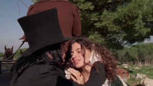 Cinematic still from the 1989 Italian biographical drama Paganini featuring a passionate outdoor embrace and kiss between a man in a tall black top hat and a woman in period attire.