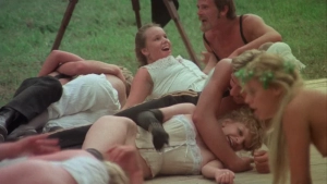 Outdoor group scene from Private Vices Public Pleasures 1976 - Multiple individuals in varied states of undress interact on a wooden platform with grassy surroundings.