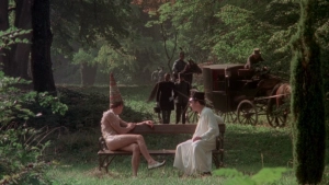 Park bench scene from Private Vices Public Pleasures (1976) - One individual wears a tall conical hat and feathered partial nude attire while conversing with another in white robes; horse-drawn carriage and riders appear in the forested background. - img #1
