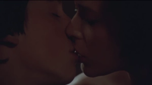 Extreme close-up from Private Lessons (1981) capturing a passionate kiss with full frontal lip contact betweenSylvia Kristel and Eric Brown in a dimly lit, shadowy room.