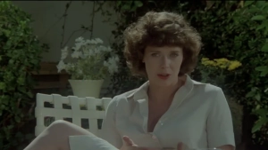 Close-up of actress Sylvia Kristel in an intimate conversation scene from *Private Lessons* (1981), wearing her signature short, curly hairstyle. She is seated outdoors at a glass patio table, engaged in a focused discussion with the young man across from her. - img #8