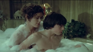 Intimate close-up from Private Lessons (1981) showing Sylvia Kristel seated in a bubble bath behind a young man, their bodies partially submerged together under thick foam.