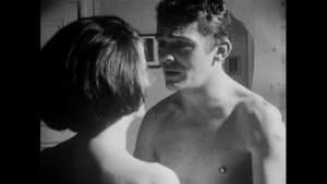 Vintage black-and-white close-up from Seeds of Sin featuring a shirtless man looking at another person from behind in an intimate indoor scene, capturing the raw and tactile aesthetic typical of 1960s erotic cinema.