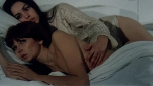 Nude and topless intimate bed scene from The Hot Nights of Linda (1975) - two women embracing on white sheets with soft indoor lighting.