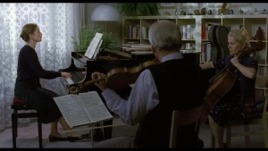 Isabelle Huppert plays piano with musicians in a living room setting, partial nudity scene from The Piano Teacher (2001). - img #1