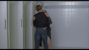 Intimate embrace between Isabelle Huppert and male lead in a tiled bathroom hallway from The Piano Teacher (2001).