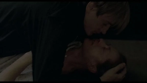 Benno Fürmann kneels beside Isabelle Huppert on a bed in an intimate bedroom scene from The Piano Teacher (2001).