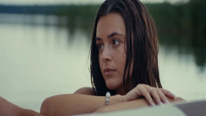 Katrina Kreile in Vulgar (2024) — wet, dark hair and bare shoulders as she gazes thoughtfully away from the camera beside a calm lake